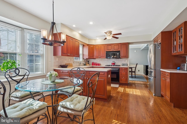 kitchen featuring tasteful backsplash, glass insert cabinets, light countertops, wood finished floors, and black appliances