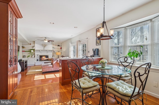 dining space with built in features, baseboards, light wood finished floors, ceiling fan, and a glass covered fireplace