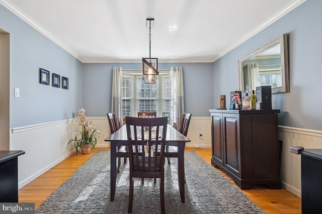 dining room with plenty of natural light, a wainscoted wall, light wood finished floors, and ornamental molding