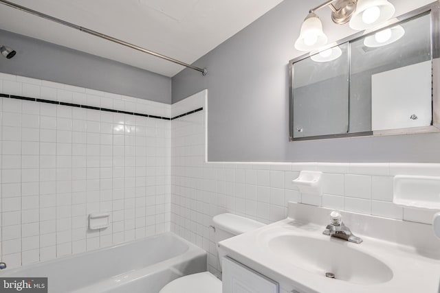 bathroom featuring toilet, tile walls, wainscoting, washtub / shower combination, and vanity