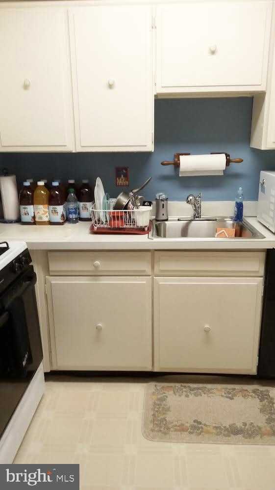 kitchen with a sink, stove, white cabinetry, light countertops, and white microwave