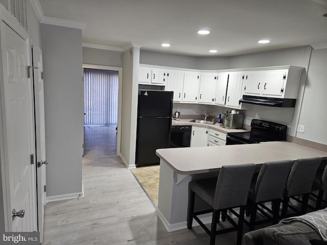 kitchen featuring light countertops, a peninsula, exhaust hood, black appliances, and a sink