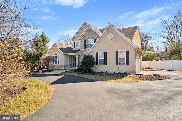 view of front of home featuring stucco siding, stone siding, driveway, and fence