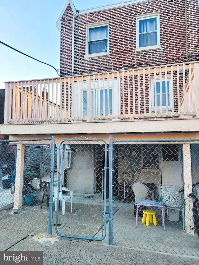 rear view of house featuring a balcony, a gate, fence, and brick siding