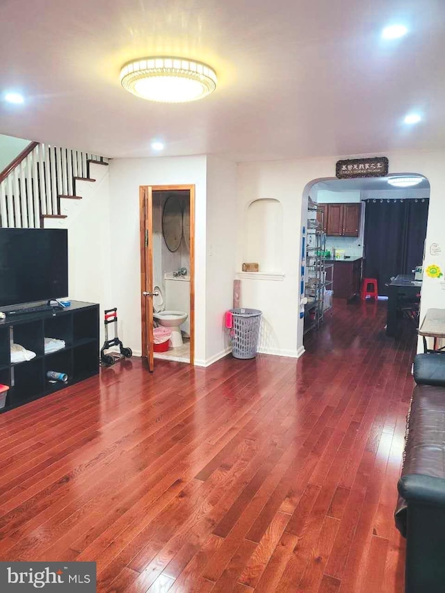 living area with arched walkways, hardwood / wood-style flooring, recessed lighting, baseboards, and stairway