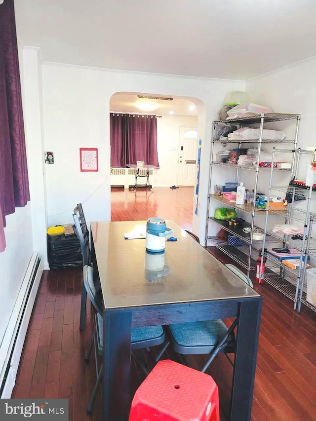 dining area featuring a baseboard heating unit, arched walkways, and dark wood-style floors