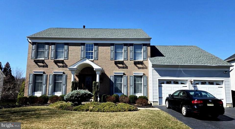 colonial house featuring aphalt driveway, a front yard, a shingled roof, a garage, and brick siding