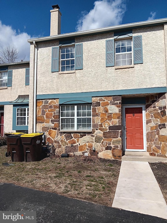 multi unit property featuring stone siding, a chimney, and stucco siding