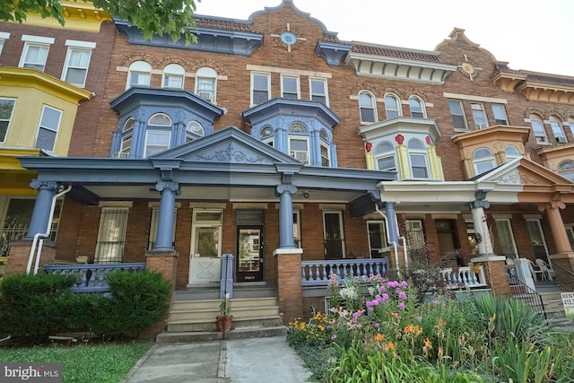 townhome / multi-family property with a porch and brick siding