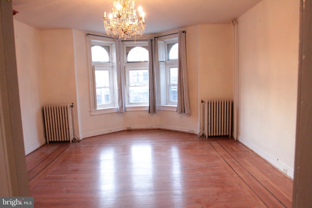 spare room featuring radiator, a notable chandelier, baseboards, and wood finished floors