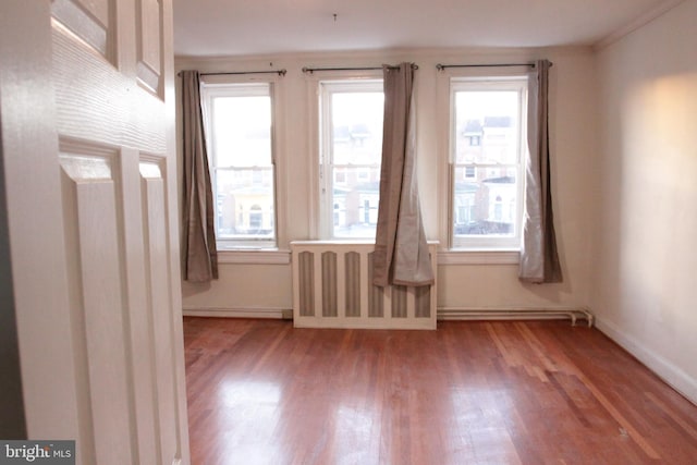 empty room featuring radiator heating unit, wood finished floors, and baseboards