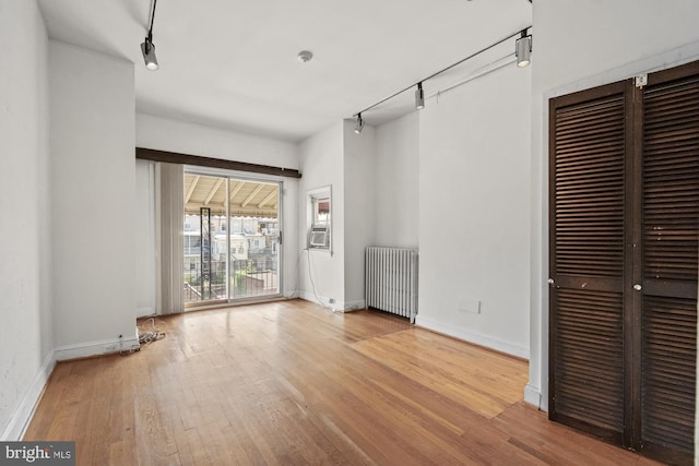 interior space with radiator heating unit, track lighting, baseboards, and wood finished floors