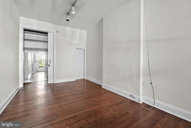 empty room with dark wood-type flooring, rail lighting, and baseboards