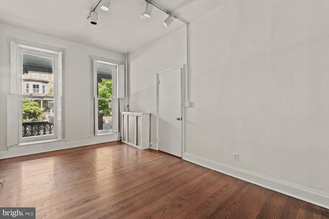 empty room featuring rail lighting, baseboards, and wood finished floors