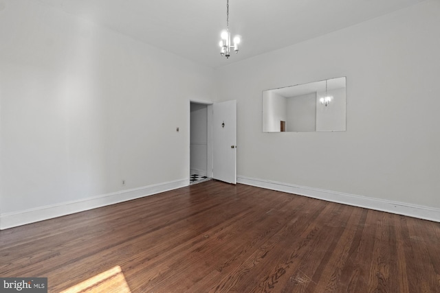 spare room featuring a chandelier, baseboards, and wood finished floors