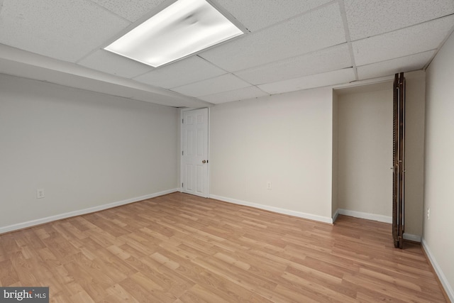 finished below grade area featuring a drop ceiling, light wood-style flooring, and baseboards