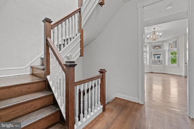 staircase with cooling unit, a notable chandelier, baseboards, and wood finished floors