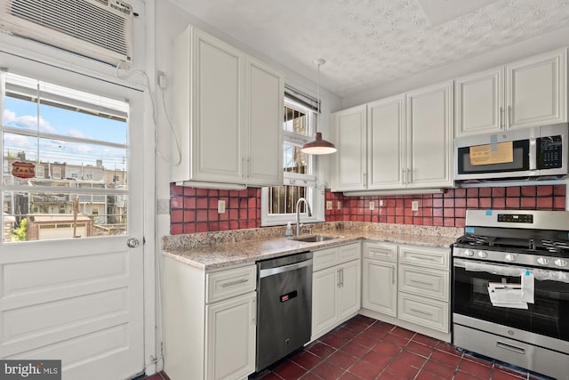 kitchen featuring a wall unit AC, backsplash, appliances with stainless steel finishes, white cabinets, and a sink