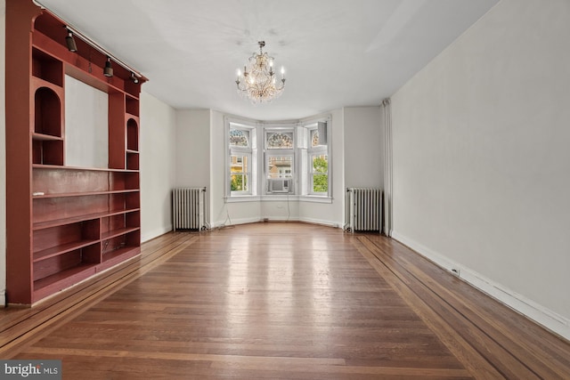 spare room with a notable chandelier, baseboards, wood finished floors, and radiator