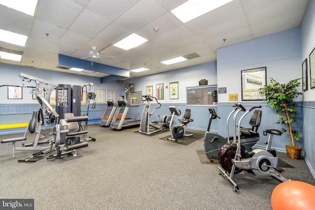 workout area with wainscoting, ceiling fan, visible vents, and a drop ceiling