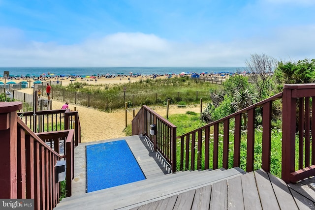 wooden terrace featuring a beach view and a water view