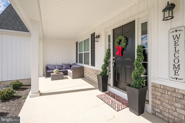 view of exterior entry featuring outdoor lounge area, roof with shingles, covered porch, and brick siding