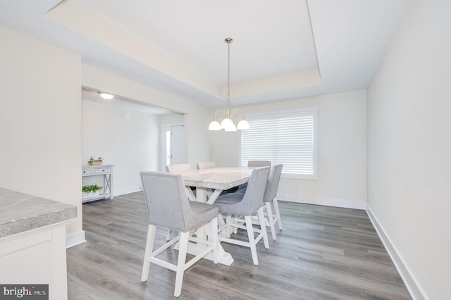 dining space with light wood finished floors, a notable chandelier, baseboards, and a tray ceiling