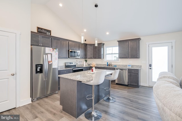 kitchen with dark brown cabinets, a center island, a kitchen bar, appliances with stainless steel finishes, and light wood-style floors