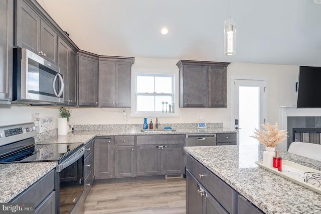 kitchen featuring dark brown cabinetry, appliances with stainless steel finishes, light stone countertops, and a sink