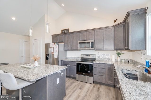 kitchen featuring a sink, appliances with stainless steel finishes, light wood finished floors, light stone countertops, and dark brown cabinets