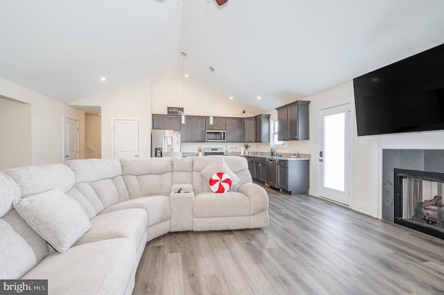 living area featuring recessed lighting, a fireplace, high vaulted ceiling, and light wood-type flooring