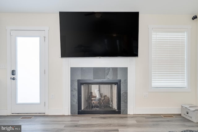 room details featuring a tiled fireplace, wood finished floors, visible vents, and baseboards