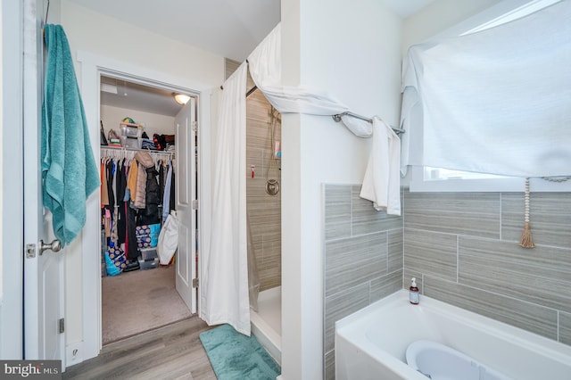 bathroom with a bath, a stall shower, a spacious closet, and wood finished floors