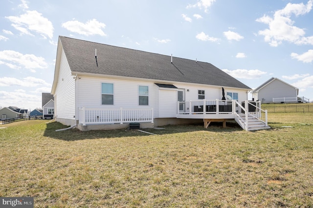 rear view of house featuring a wooden deck, a lawn, a shingled roof, and fence