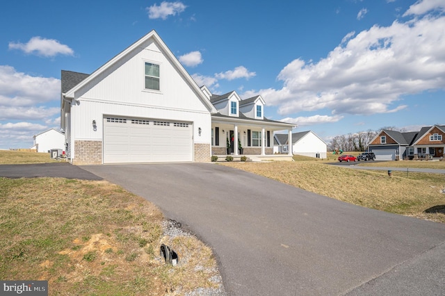 view of front facade featuring a front yard, driveway, an attached garage, covered porch, and brick siding