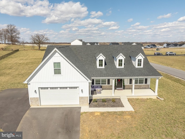 view of front of house with brick siding, a porch, a front yard, roof with shingles, and driveway