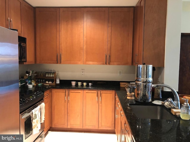 kitchen featuring appliances with stainless steel finishes, dark stone counters, brown cabinetry, and a sink