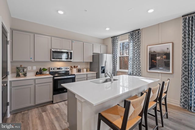 kitchen with gray cabinetry, stainless steel appliances, a sink, a kitchen breakfast bar, and light wood-type flooring