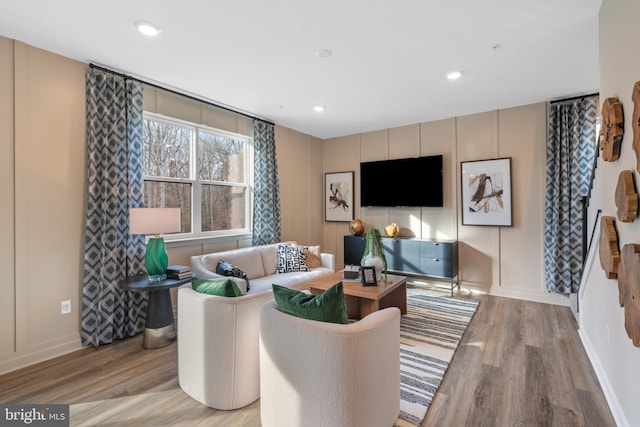 living area with light wood-style floors, baseboards, a decorative wall, and recessed lighting