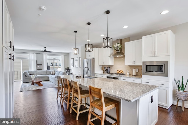 kitchen featuring dark wood-style flooring, stainless steel appliances, a barn door, wall chimney exhaust hood, and open floor plan