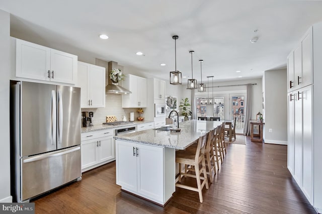 kitchen with dark wood-type flooring, a kitchen island with sink, a sink, appliances with stainless steel finishes, and white cabinets