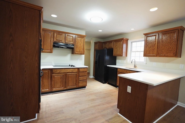 kitchen featuring a peninsula, under cabinet range hood, black appliances, and light wood finished floors