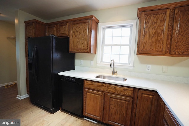 kitchen featuring light wood-style flooring, brown cabinets, light countertops, black appliances, and a sink