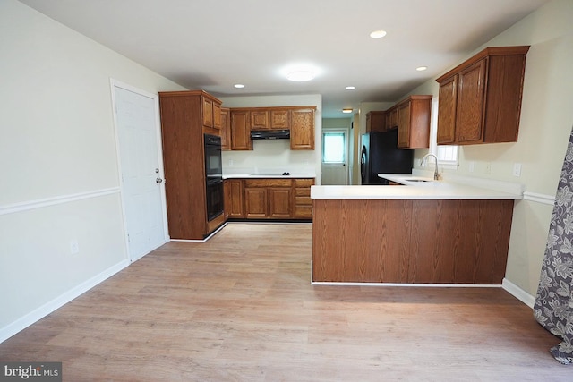 kitchen featuring brown cabinets, a peninsula, under cabinet range hood, light wood-type flooring, and black appliances