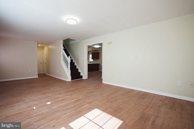 spare room featuring stairs, light wood finished floors, and baseboards