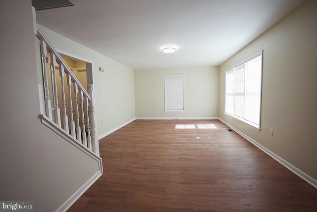 empty room featuring baseboards, stairway, and wood finished floors