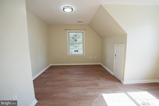 additional living space with visible vents, vaulted ceiling, baseboards, and wood finished floors