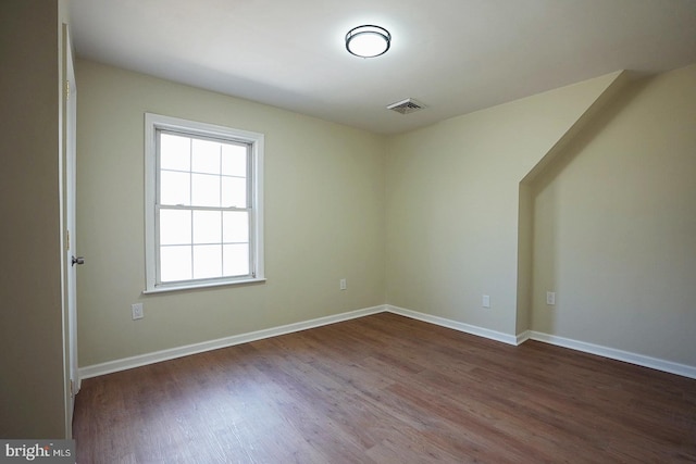 spare room with dark wood-style floors, visible vents, and baseboards