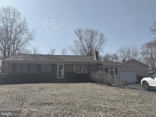 single story home featuring brick siding, a chimney, a front yard, a garage, and driveway