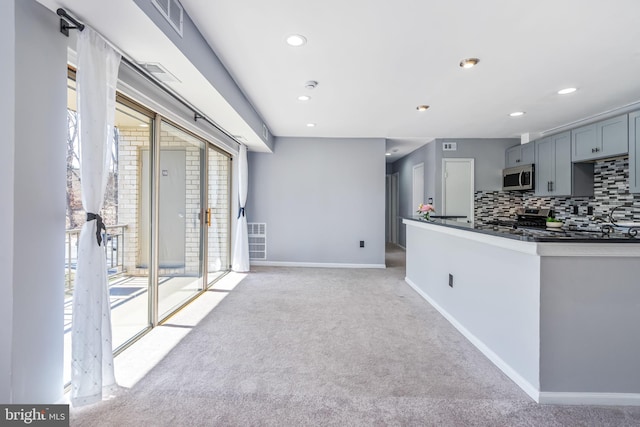 kitchen with dark countertops, baseboards, light carpet, stainless steel microwave, and tasteful backsplash